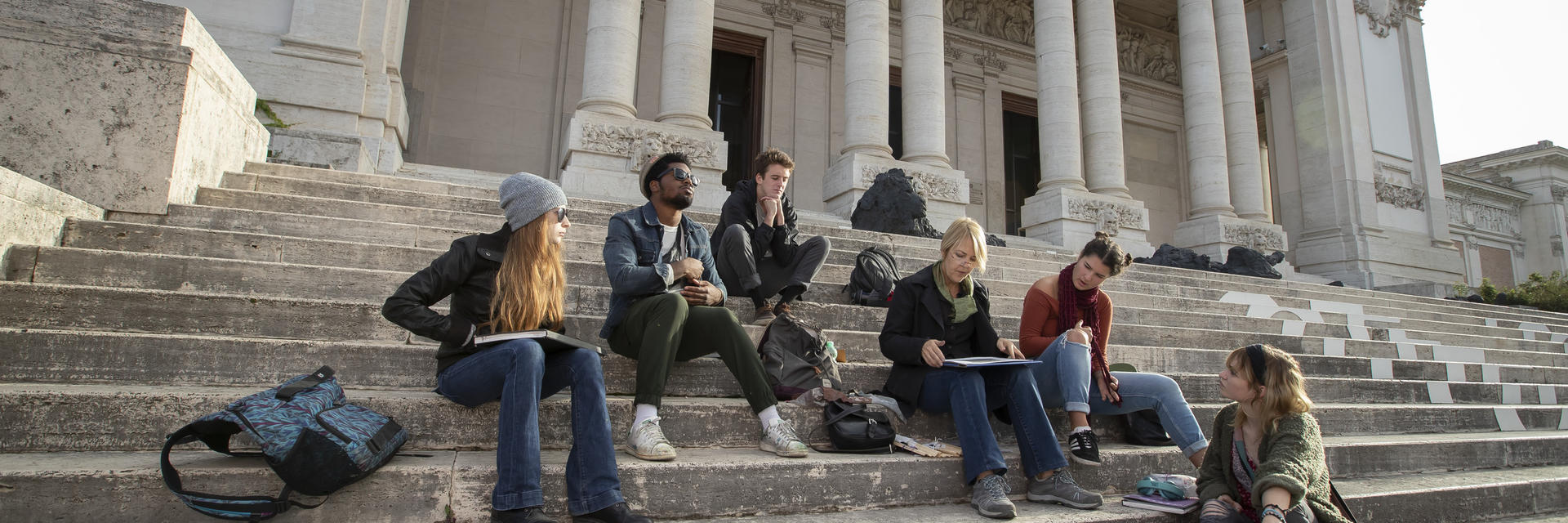 Students sit on the steps of a classical building in Rome.